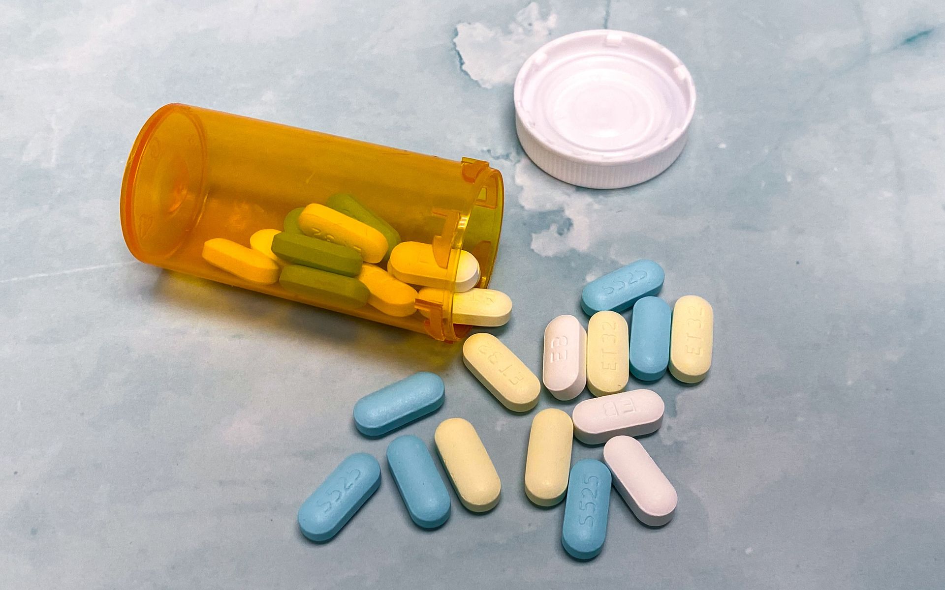 An open prescription bottle with assorted pills on a light blue background, high angle view.