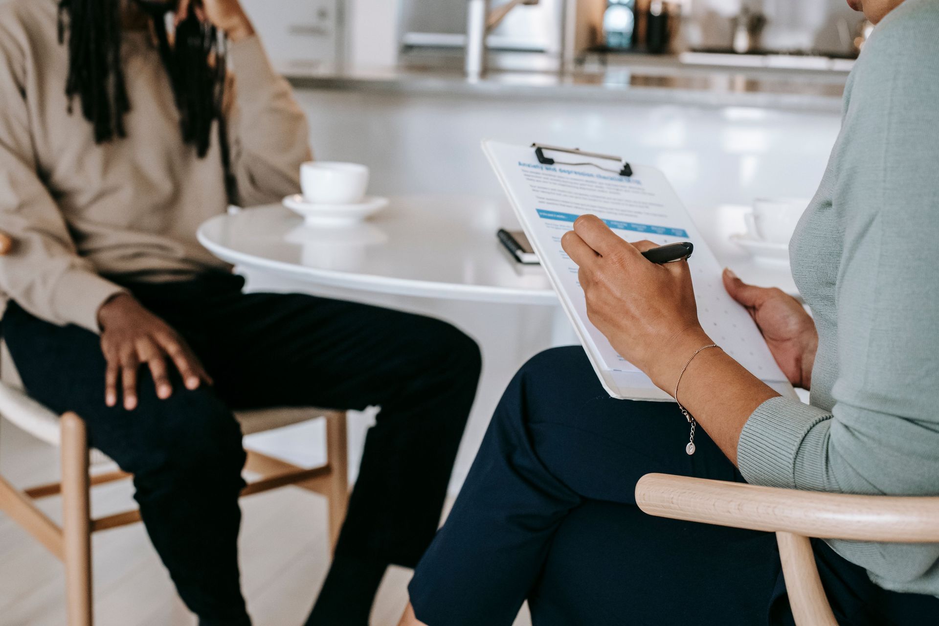 Crop unrecognizable female psychotherapist or interviewer asking questions and taking notes in clipboard during interview with black male